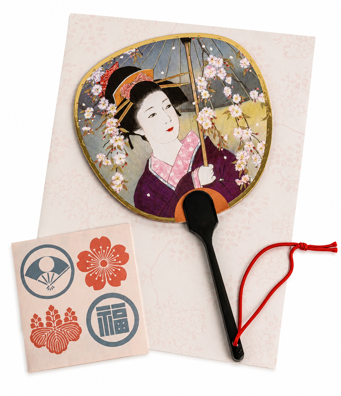 Japanese geisha fan greetings card featuring a geisha beneath cherry blossoms with gold border and red tassel cord