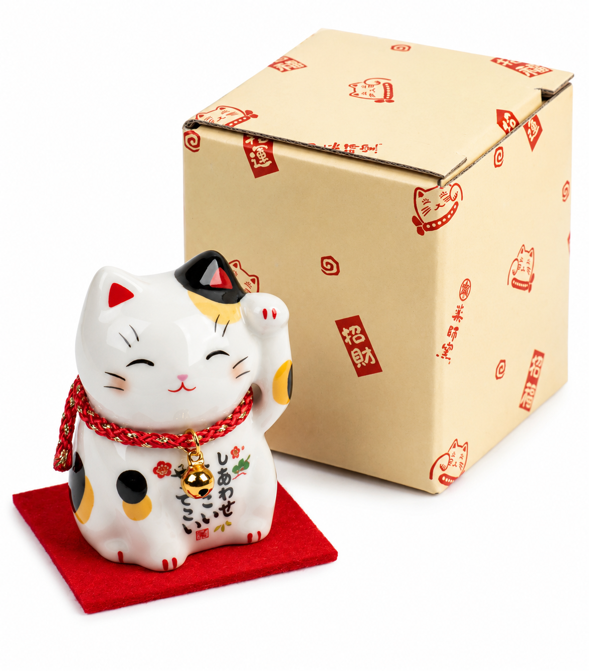Calico Maneki Neko lucky cat figurine with raised paw and gold bell beside its Yakushido gift box printed with red lucky cat motifs and kanji, seated on red felt mat