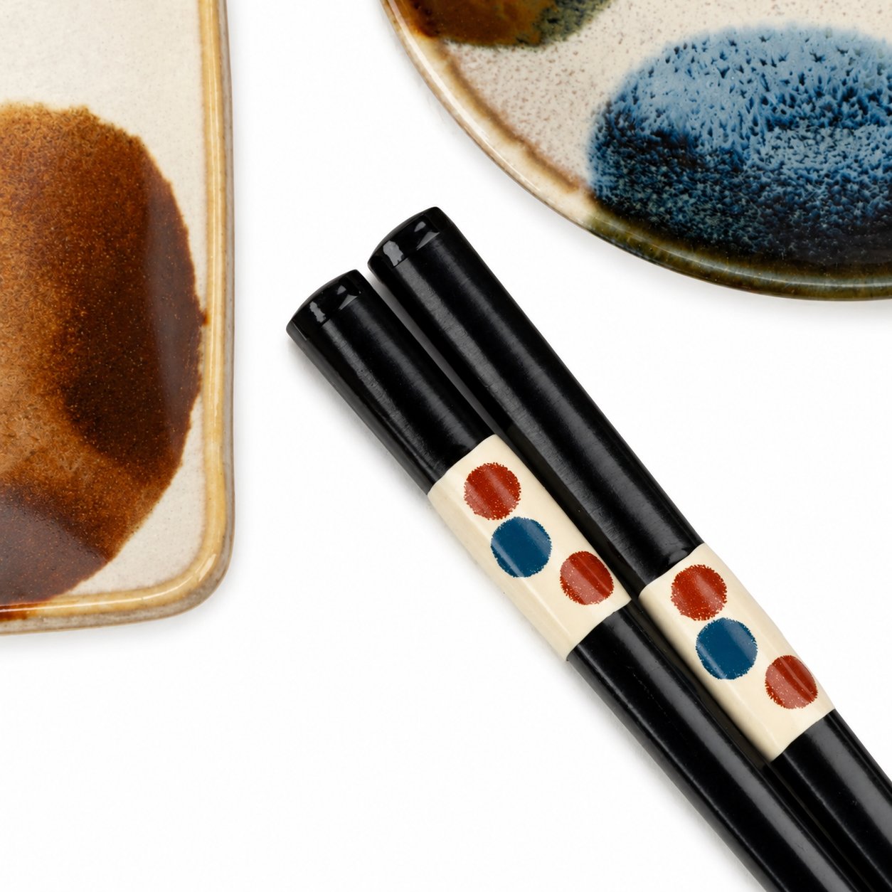 Black lacquer chopsticks with red and blue dot pattern on cream band, displayed alongside ceramic sushi plates with blue and brown dot glaze pattern.