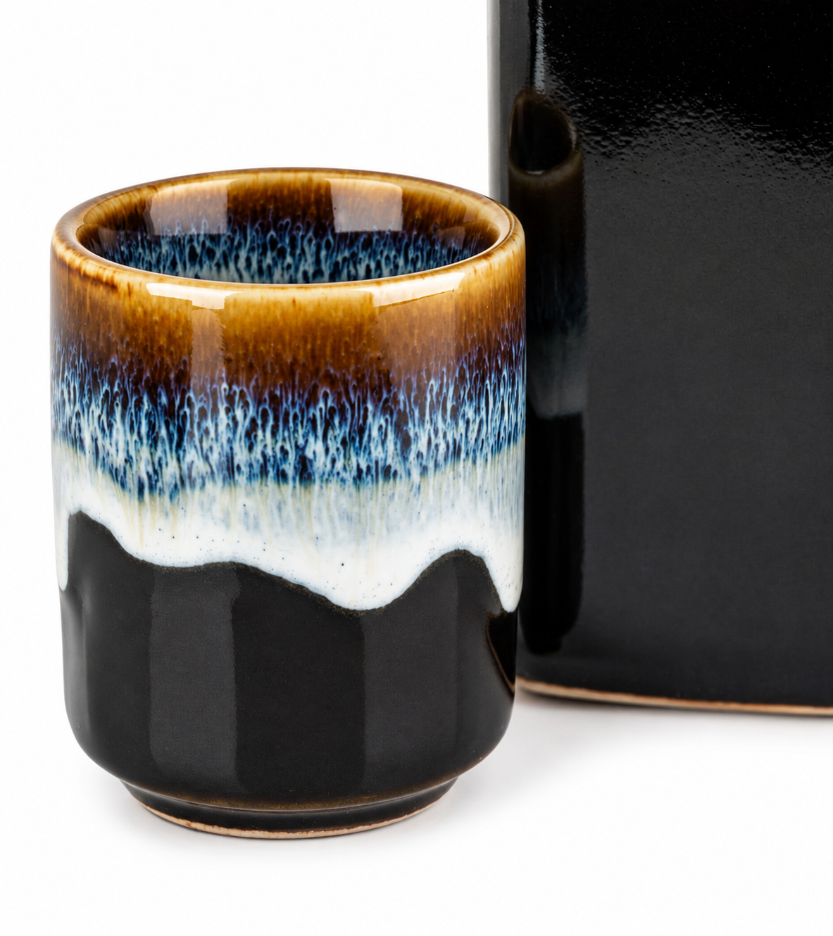Close-up of Yoru sake cup showing amber, blue and white layered drip glaze on black ceramic, made in Japan